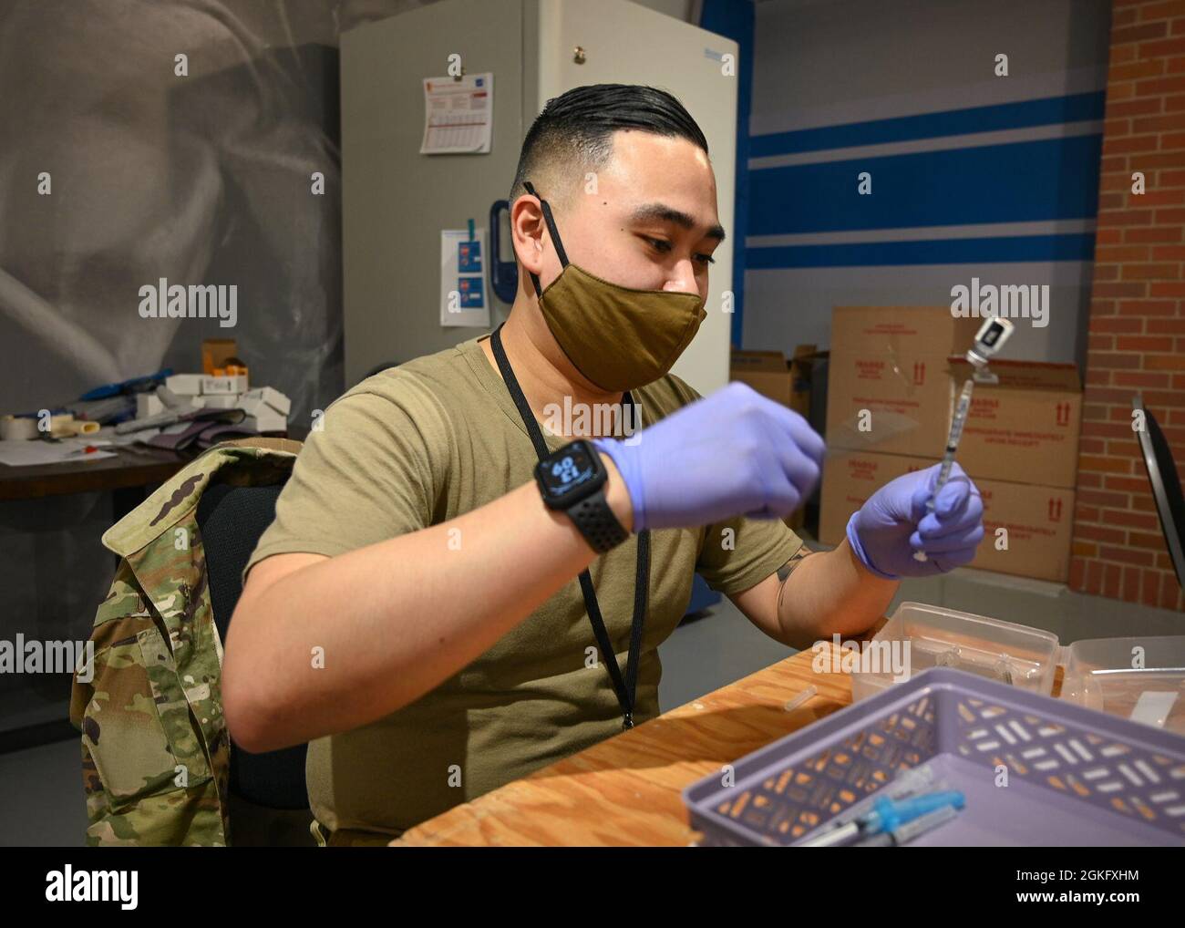 U.S. Air Force Senior Airman Vincent Uy, a Los Banos, California native and laboratory technician with the 88th Diagnostics Squadron, 88th Air Base Wing stationed at Wright-Patterson Air Force Base, removes air bubbles from a vaccine syringe to ensure a correct dose at the state-led, federally-supported Ford Field COVID-19 Community Vaccination Center in Detroit, April 12, 2021. Uy is part of a group of Airmen assigned to 1st Detachment, 64th Air Expeditionary Group that are assisting with the vaccination efforts. Uy’s main responsibility is supporting the local community members by preparing Stock Photo