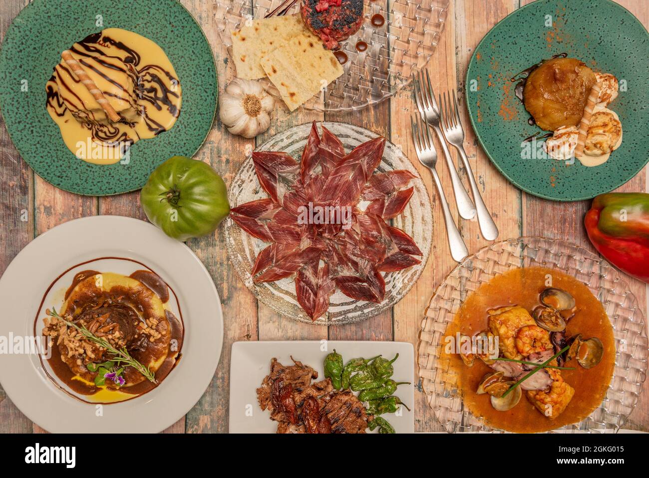 Set of plates of homemade food and jabugo ham with forks, hake with seafood, entrecote chopped with padron peppers, pork cheek with potato cream. Stock Photo