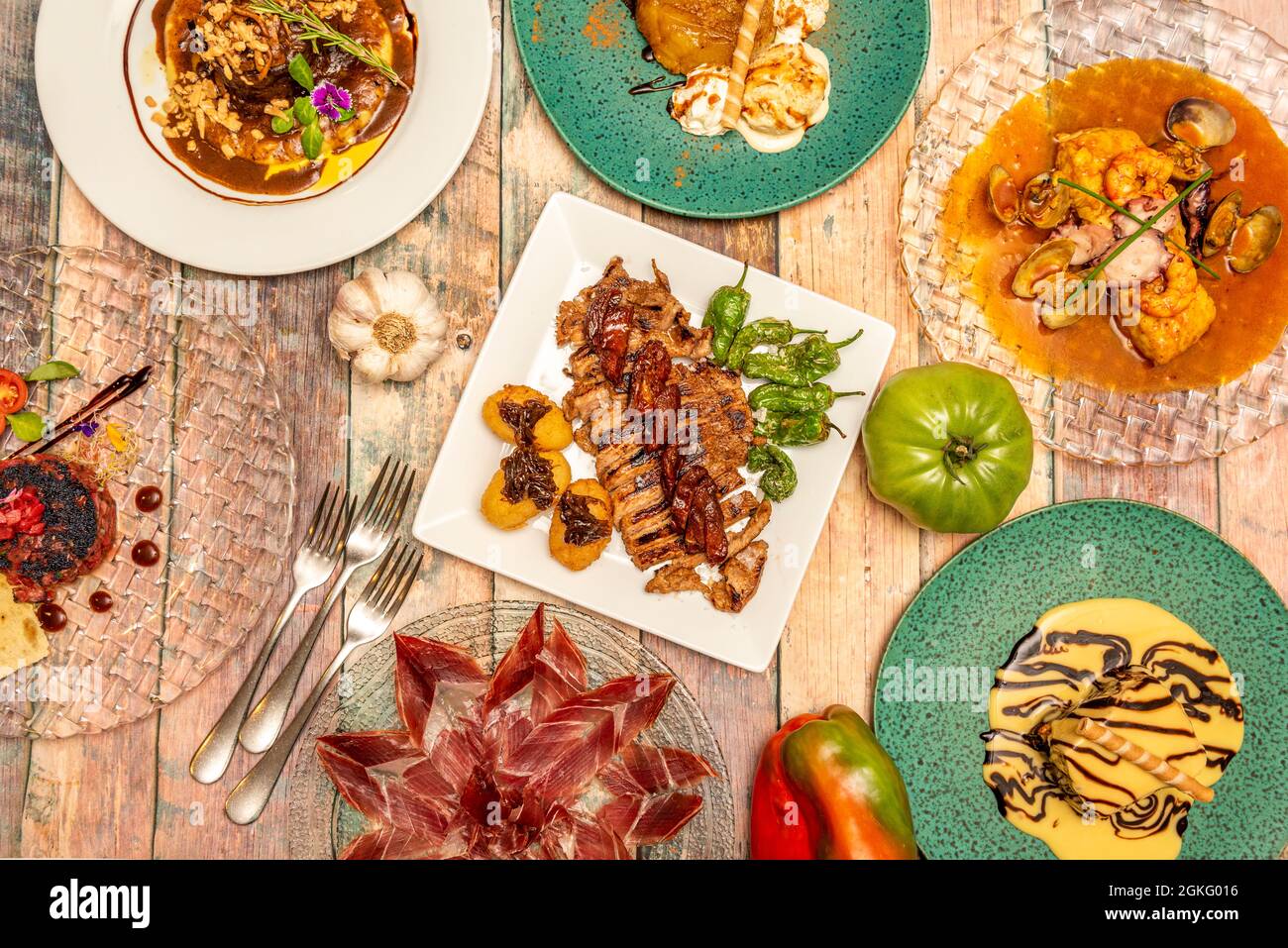 popular dishes of Spanish gastronomy: hake in marine sauce, acorn-fed Iberian ham, roast tenderloin with peppers and potatoes, tomatoes, garlic, peppe Stock Photo