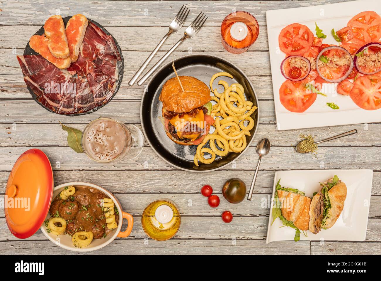 Set of dishes of Spanish food and hamburgers. Meatballs in sauce, acorn-fed Iberian ham, tomato salad, pastrami sandwich Stock Photo