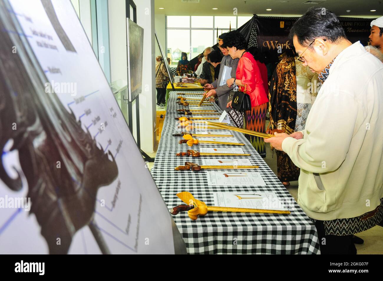 People are observing kris or keris, a type of traditional dagger, displayed on a long table. Stock Photo