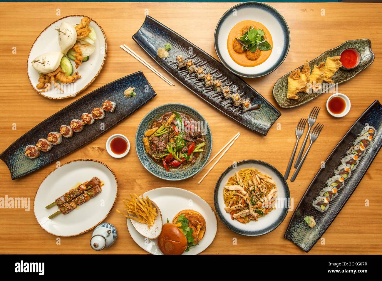 Set of beautiful asian food dishes on wooden table. Uramaki, tempura crab dip, fried gyozas, bluefin tuna skewer, stir-fry noodles, beef stew with veg Stock Photo