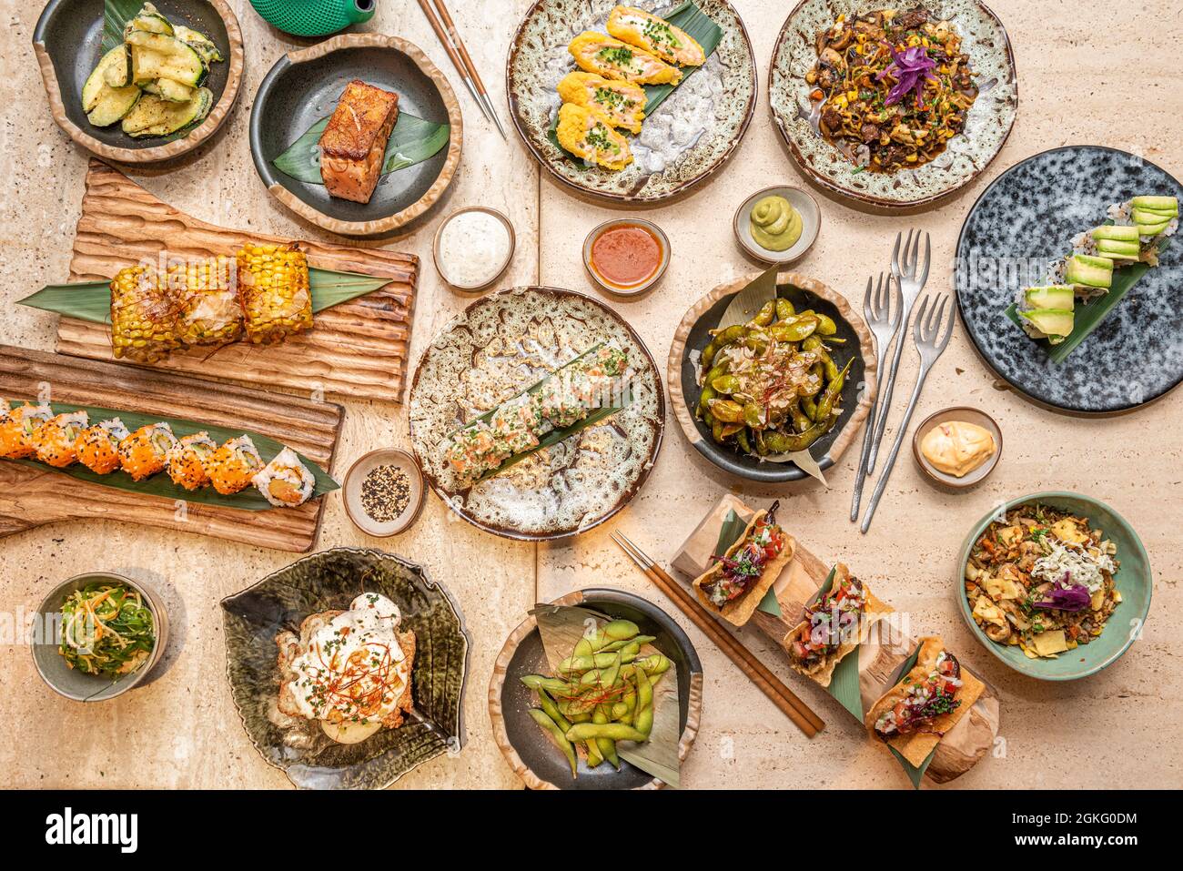 Asian food dishes on a marble table. edamame, california roll, uramaki salmon, seafood tacos, soy sauce, sesame, corn, salmon. Stock Photo