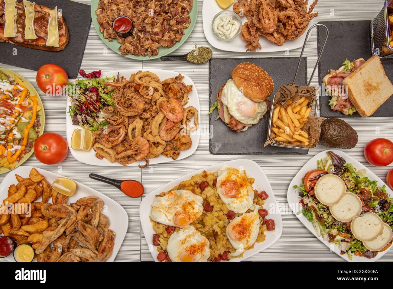 Top view image of popular Spanish dishes and tapas. Fried wings, squid squid, squid sandwich, chicken sandwich, salad with anchovies. Stock Photo