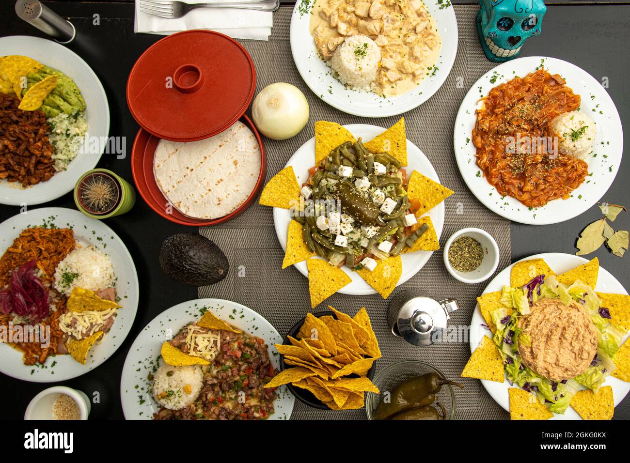 Top view image of Mexican food dishes.  Nachos with nopales, chicken tinga, chili con carne, whole jalapeños, corn cakes, purple onion, pumpkin flower Stock Photo