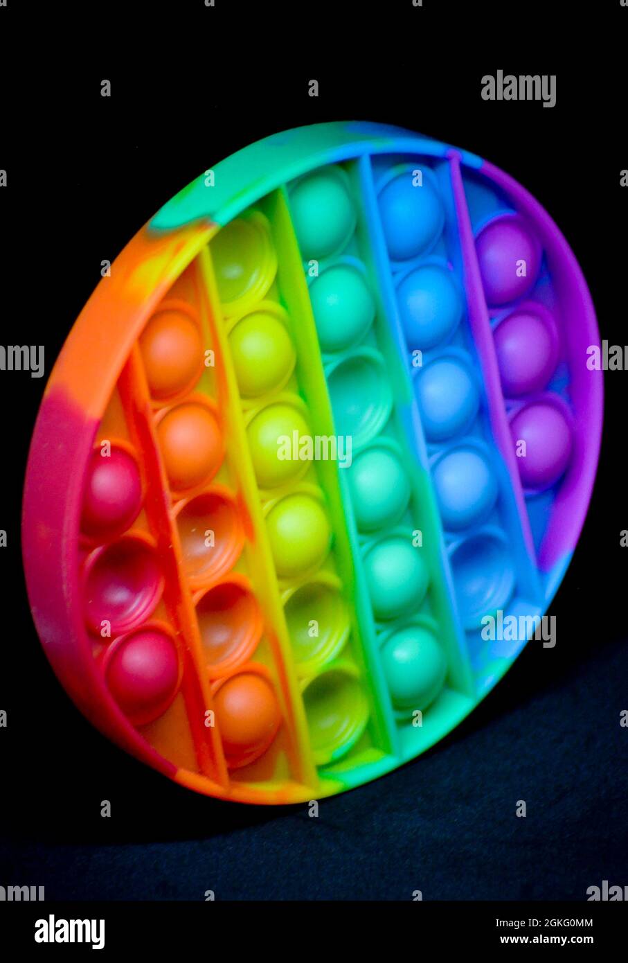 Rainbow coloured fidget popper toy to help relieve anxiety or sensory difficulties in children. Image is set against a black background Stock Photo