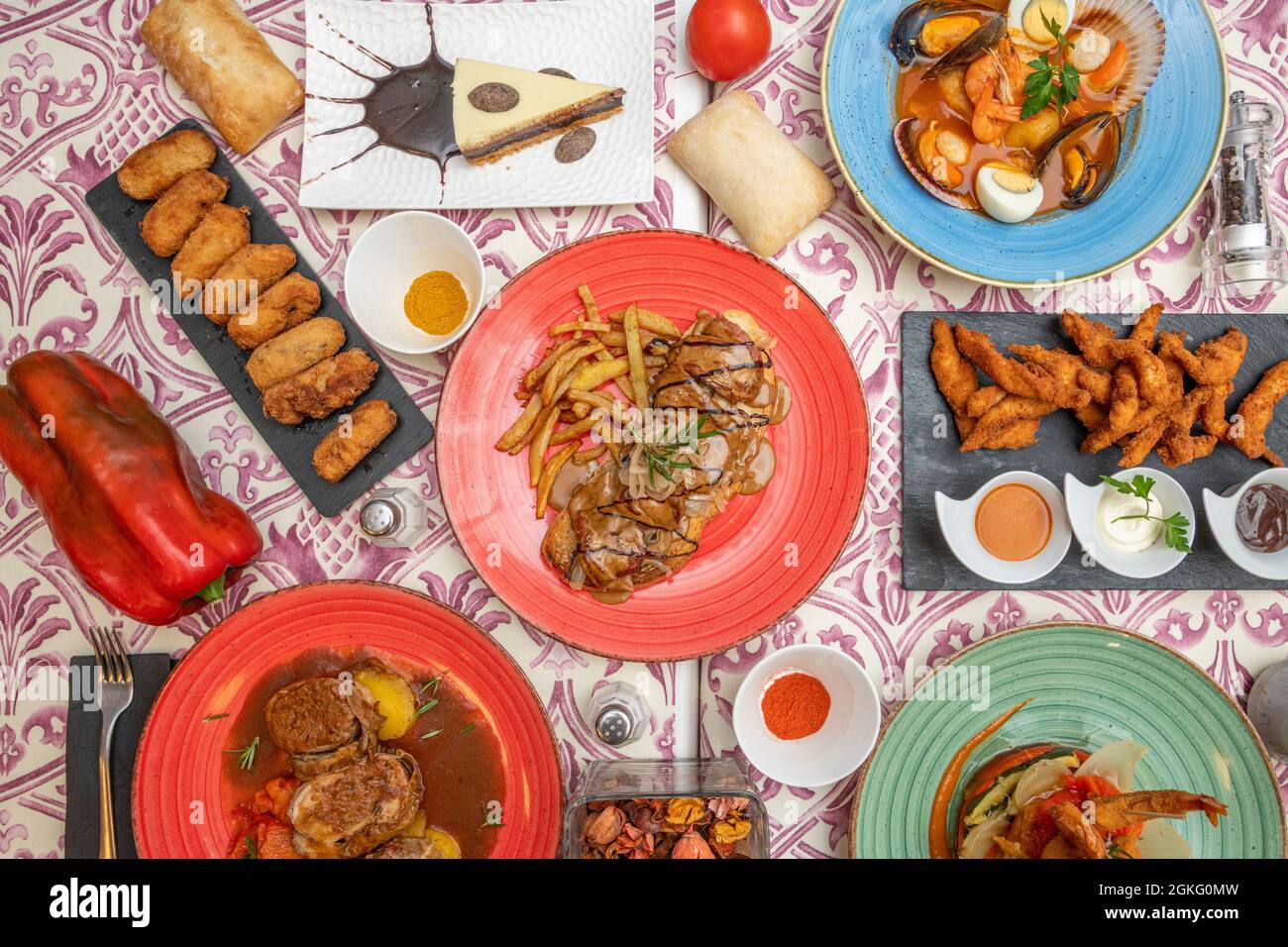 top view image of Spanish food dishes. Ham croquettes, seafood soup, pepper steak, pork cheek, paprika, bread, pepper. Stock Photo