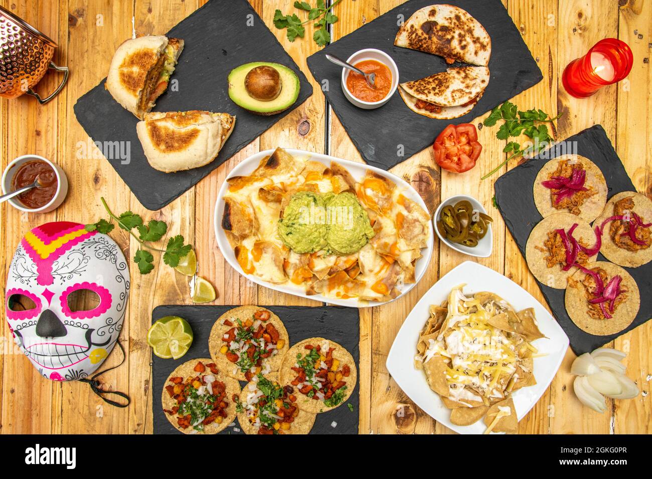 Top view image of set of Mexican dishes and catrina mask. Cochinita pibil tacos, pastor tacos, nachos with guacamole, quesadillas, jalapeños, limes an Stock Photo