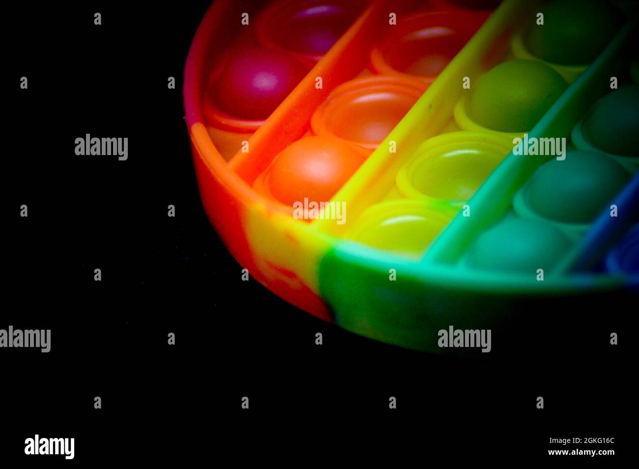 Rainbow coloured fidget popper toy to help relieve anxiety or sensory difficulties in children. Image is set against a black background Stock Photo