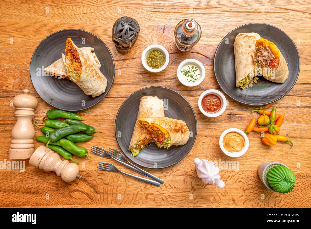 Top view image of Mexican burritos with peppers, sauces, fresh pepper, black skull and forks Stock Photo