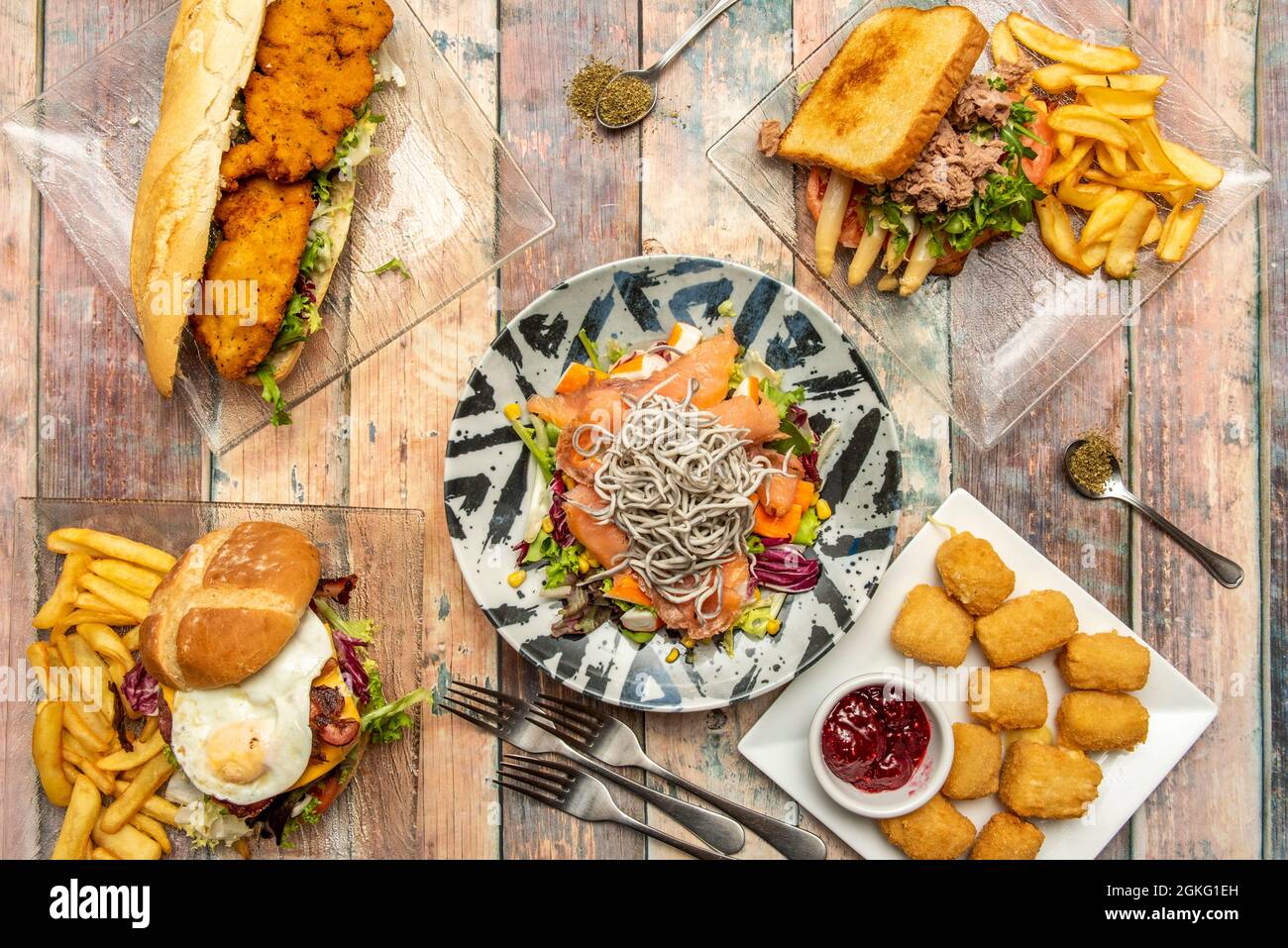 Freshly made food set. Seafood salad with salmon, eel and surimi, tuna and asparagus sandwich, chicken nuggets, breaded chicken sandwich and forks and Stock Photo