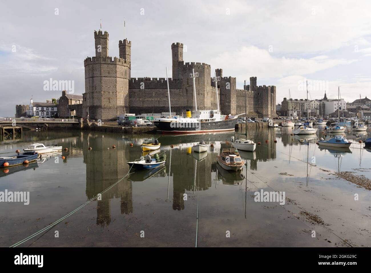 Caernarfon, Gwynedd, UK, September 9th 2021: Edward I's castle reflected in the harbour in which are moored small boats and ex-lightship Britain. Stock Photo