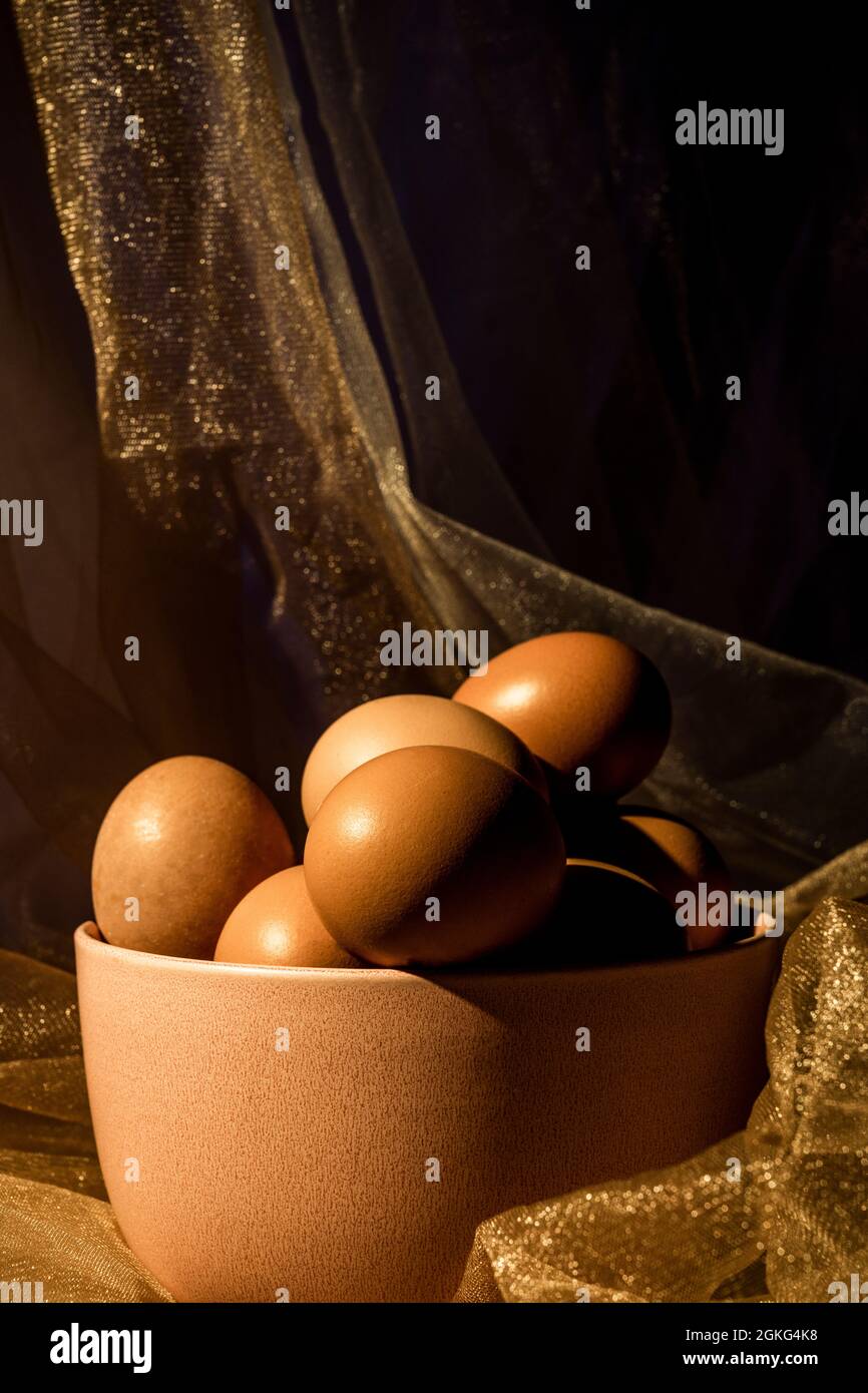 bowl of raw pink eggs with tulle fabric with golden reflections. Stock Photo