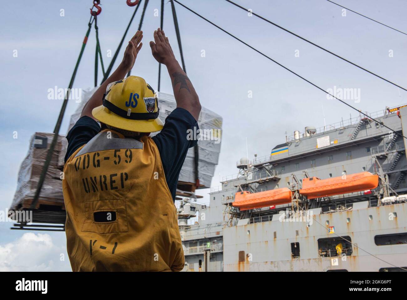 PACIFIC OCEAN (April 14, 2021) U.S. Navy Boatswain’s Mate Seaman Juan Silva, from Defiance, Ohio, signals the Lewis and Clark-class dry cargo and ammunition ship USNS Amelia Earhart (T-AKE 6) while receiving cargo aboard the Arleigh Burke-class guided-missile destroyer USS Russell (DDG 59) during a replenishment-at-sea April 14, 2021. Russell, part of the Theodore Roosevelt Carrier Strike Group, is on a scheduled deployment to the U.S. 7th Fleet area of operations. As the U.S. Navy’s largest forward-deployed fleet, 7th Fleet routinely operates and interacts with 35 maritime nations while condu Stock Photo