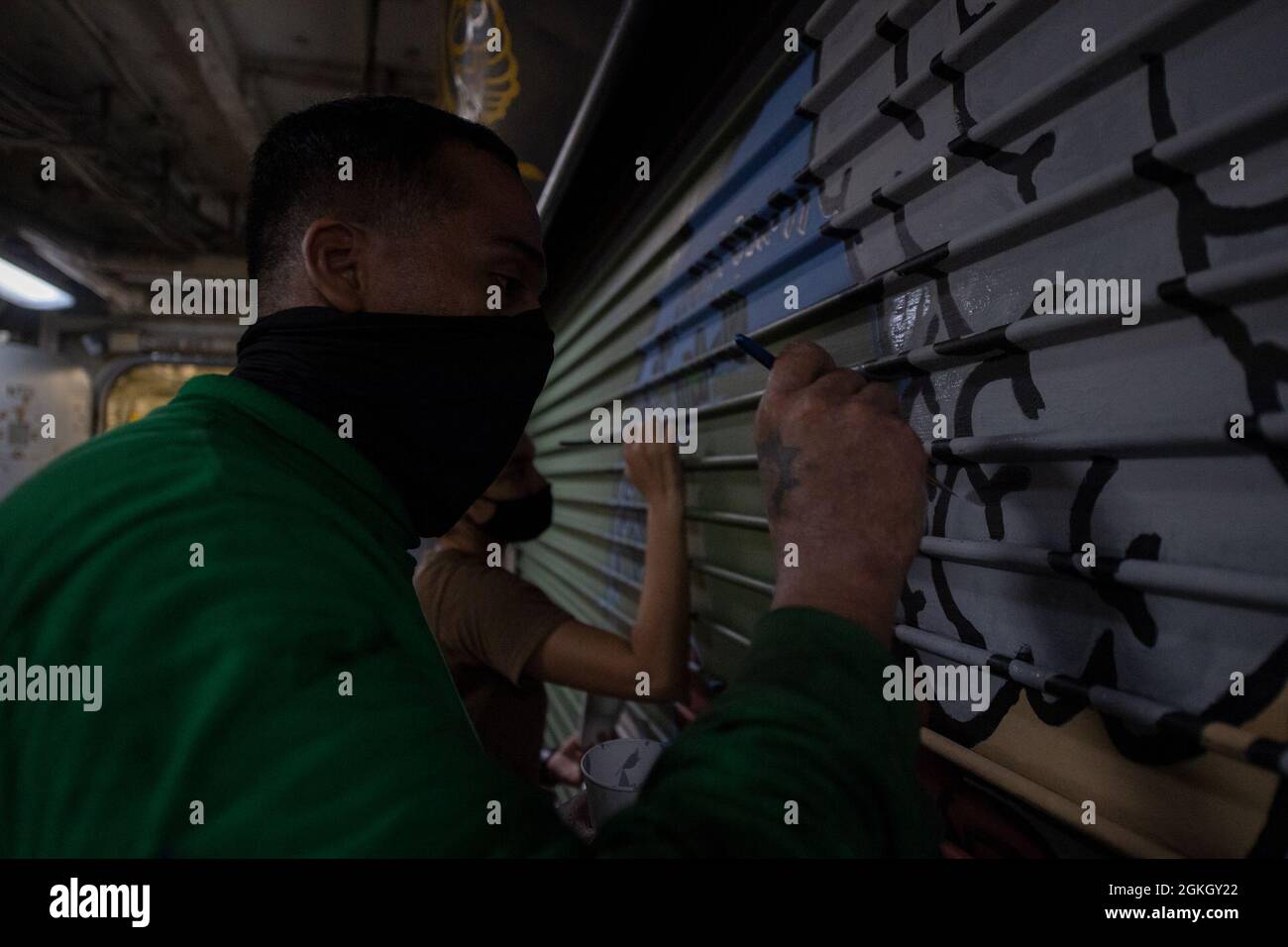 PACIFIC OCEAN (April 19, 2021) – U.S. Navy Aviation Support Equipment Technician 3rd Class Adam Hill, from San Jose, Calif., front, and Aviation Support Equipment Technician 3rd Class Paola Navarro, from Carolina, Puerto Rico, paint a mural aboard the aircraft carrier USS Theodore Roosevelt (CVN 71) April 19, 2021. The Theodore Roosevelt Carrier Strike Group is on a scheduled deployment to the U.S. 7th Fleet area of operations. As the U.S. Navy’s largest forward-deployed fleet, 7th Fleet routinely operates and interacts with 35 maritime nations while conducting missions to preserve and protect Stock Photo