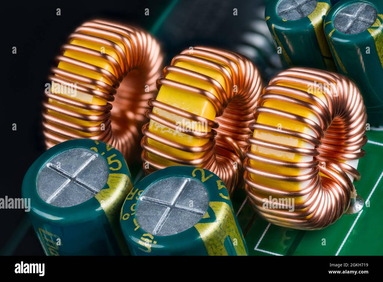 Yellow ferrite cores of toroidal inductors wrapped with copper wire on green printed circuit board. Closeup of coils or electrolytic capacitors on PCB. Stock Photo