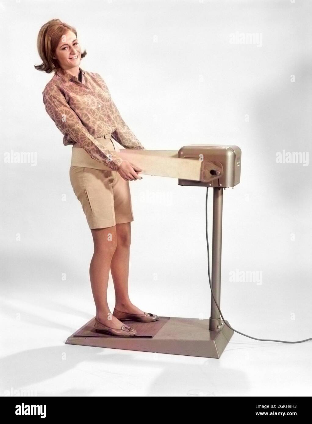 1960s SMILING YOUNG WOMAN STANDING ON WEIGHT REDUCING VIBRATING EXERCISE MACHINE LOOKING AT CAMERA - g6509c HAR001 HARS PERSONS GROWN-UP EYE CONTACT HIPS HAPPINESS WELLNESS RECREATION VIBRATING VIBRATE GOOD HEALTH BERMUDA SHORTS REDUCING DEVICE ELECTRONIC SPORTS GYMNASTICS YOUNG ADULT WOMAN CAUCASIAN ETHNICITY HAR001 OLD FASHIONED Stock Photo