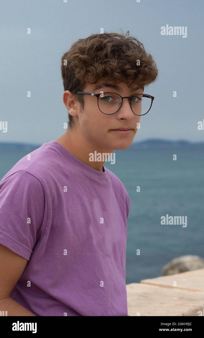 Teenage boy with glasses and curly hair poses stylishly by the sea. copy  space Stock Photo - Alamy