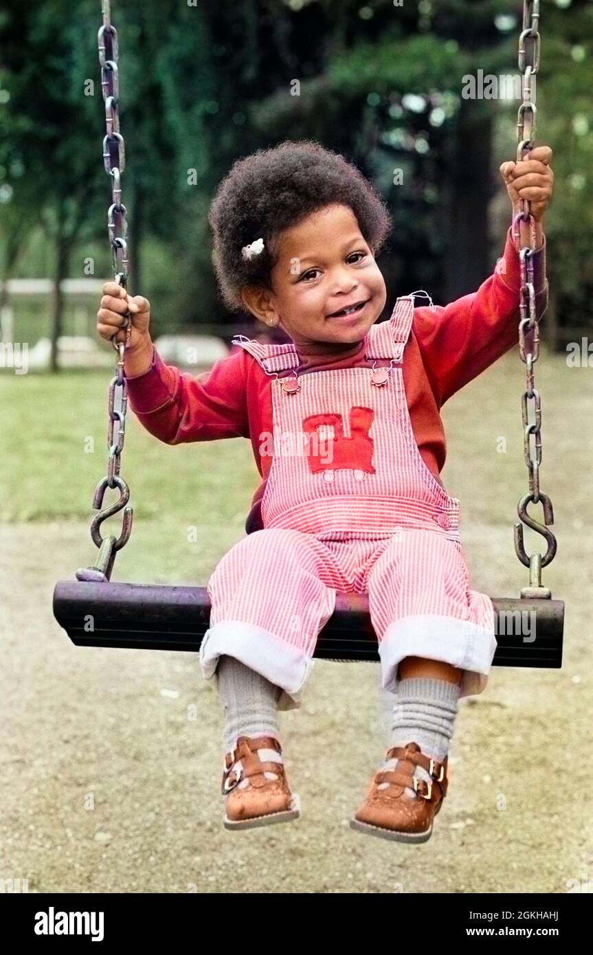 1970s 1980s CUTE CHARMING AFRICAN AMERICAN GIRL IN OVERALLS SITTING ON PLAYGROUND SWING LOOKING AT CAMERA - j14766c HAR001 HARS OVERALLS AMERICANS SINGLE FIGURE EYE CONTACT MINORITY HAPPINESS CHEERFUL AFRICAN-AMERICAN RECREATION ETHNIC DIVERSITY SMILES SWINGING BLACKS JOYFUL MINORITIES YOUNGSTER HAR001 OLD FASHIONED Stock Photo