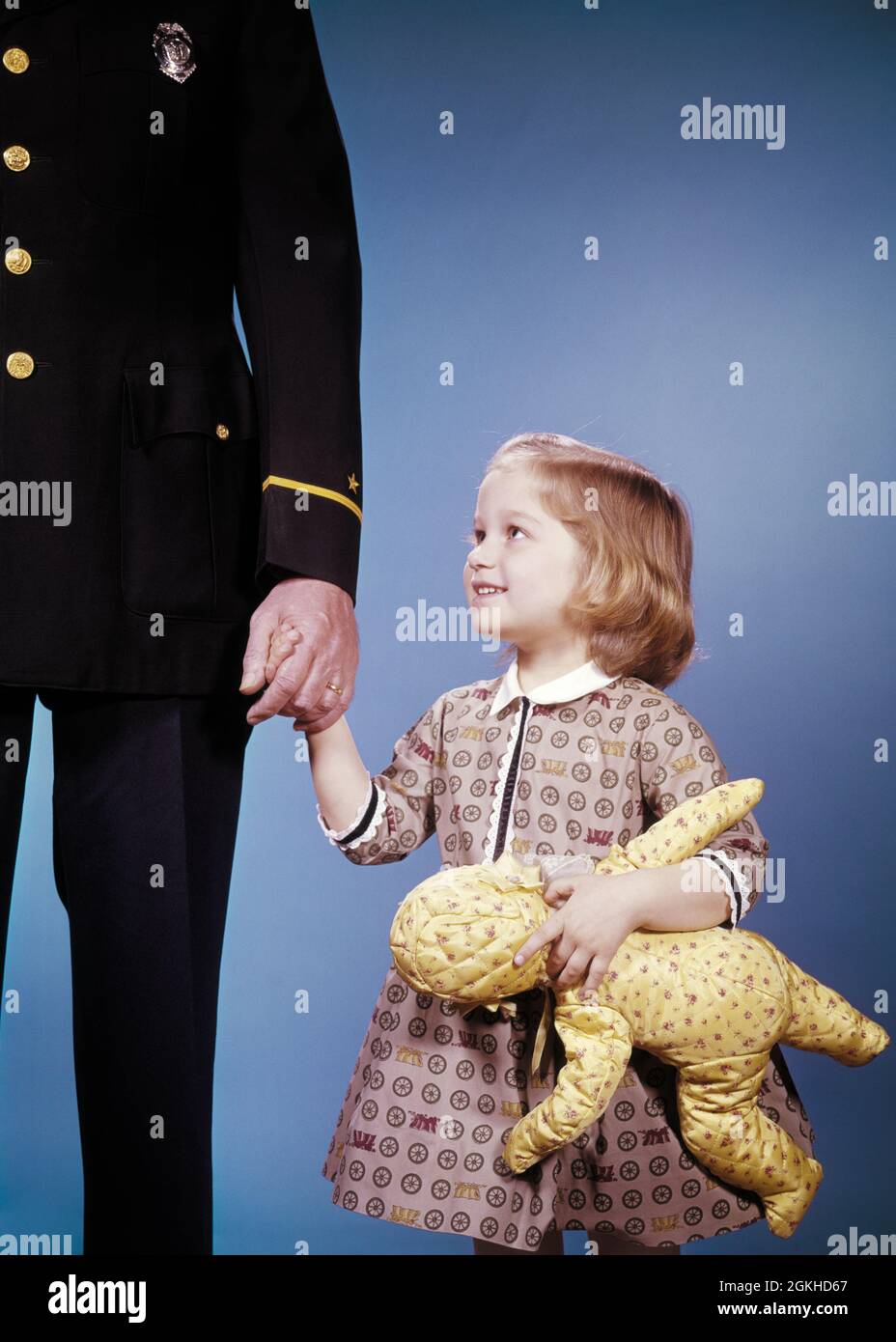 1960s LITTLE GIRL WITH YELLOW TOY DOLL HOLDING HAND OF POLICEMAN HELPING HER - kj1494 HAR001 HARS NOSTALGIA OLD FASHION 1 POLICEMAN JUVENILE FACIAL SERVE LOST PLEASED JOY LIFESTYLE FEMALES STUDIO SHOT COPY SPACE HALF-LENGTH PERSONS CARING MALES ORDER OFFICER EXPRESSIONS TRUST COP PROTECT CHEERFUL ADVENTURE AND FOUND LOW ANGLE OCCUPATIONS SMILES UNIFORMS CONCEPTUAL TRUSTING JOYFUL TRUSTWORTHY OFFICERS POLICEMEN COPS GROWTH JUVENILES MID-ADULT MID-ADULT MAN BADGE BADGES CAUCASIAN ETHNICITY HAR001 OLD FASHIONED Stock Photo