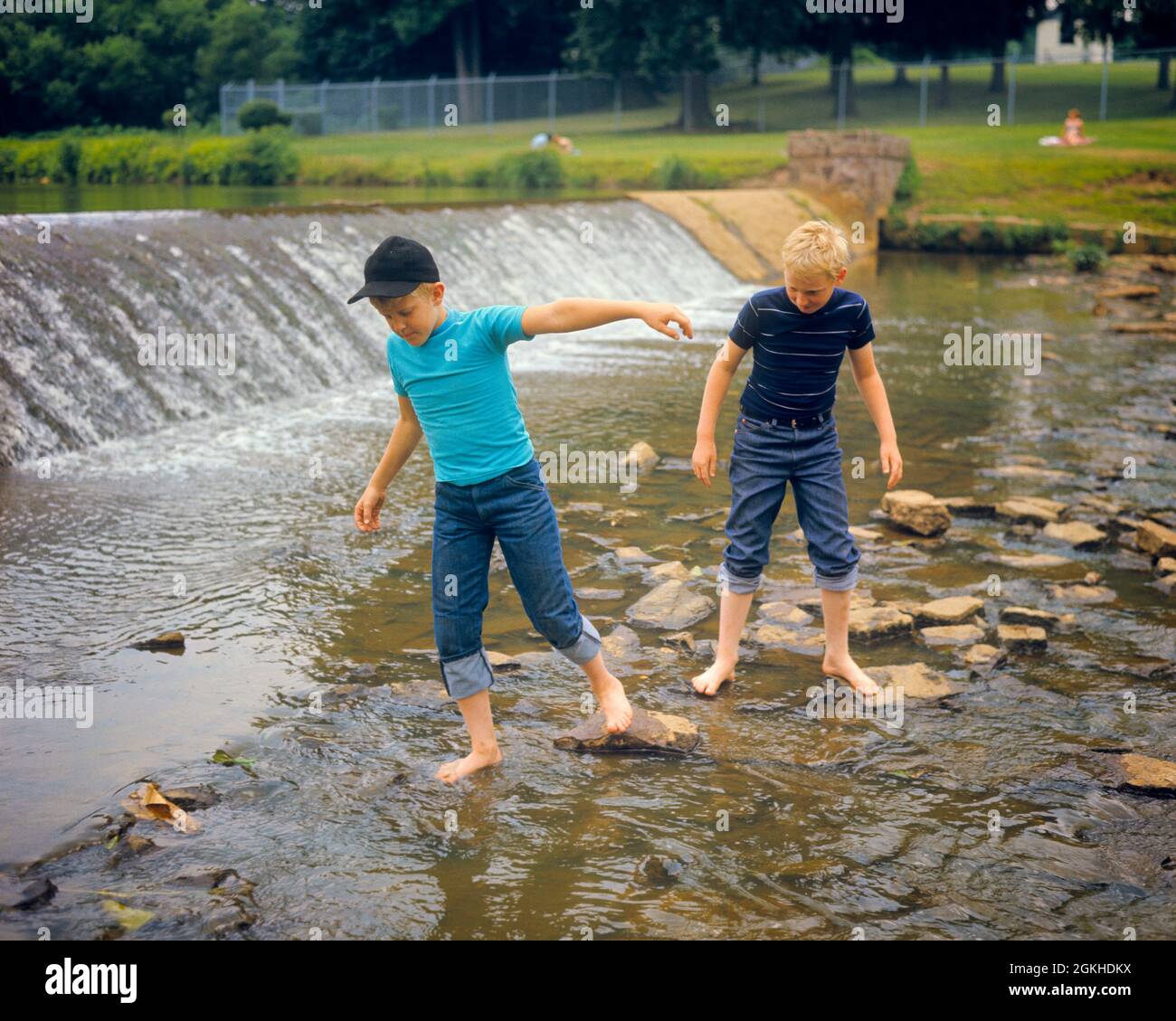 1970s TWO BOYS WADING BAREFOOT IN ROCKY STREAM JUST BELOW SPILLWAY OF A  SMALL WEIR - kj4445 HAR001 HARS JUST SIBLINGS CONFIDENCE DENIM SUMMERTIME  FREEDOM FRESH TEMPTATION ROCKY HAPPINESS ADVENTURE DISCOVERY WADING