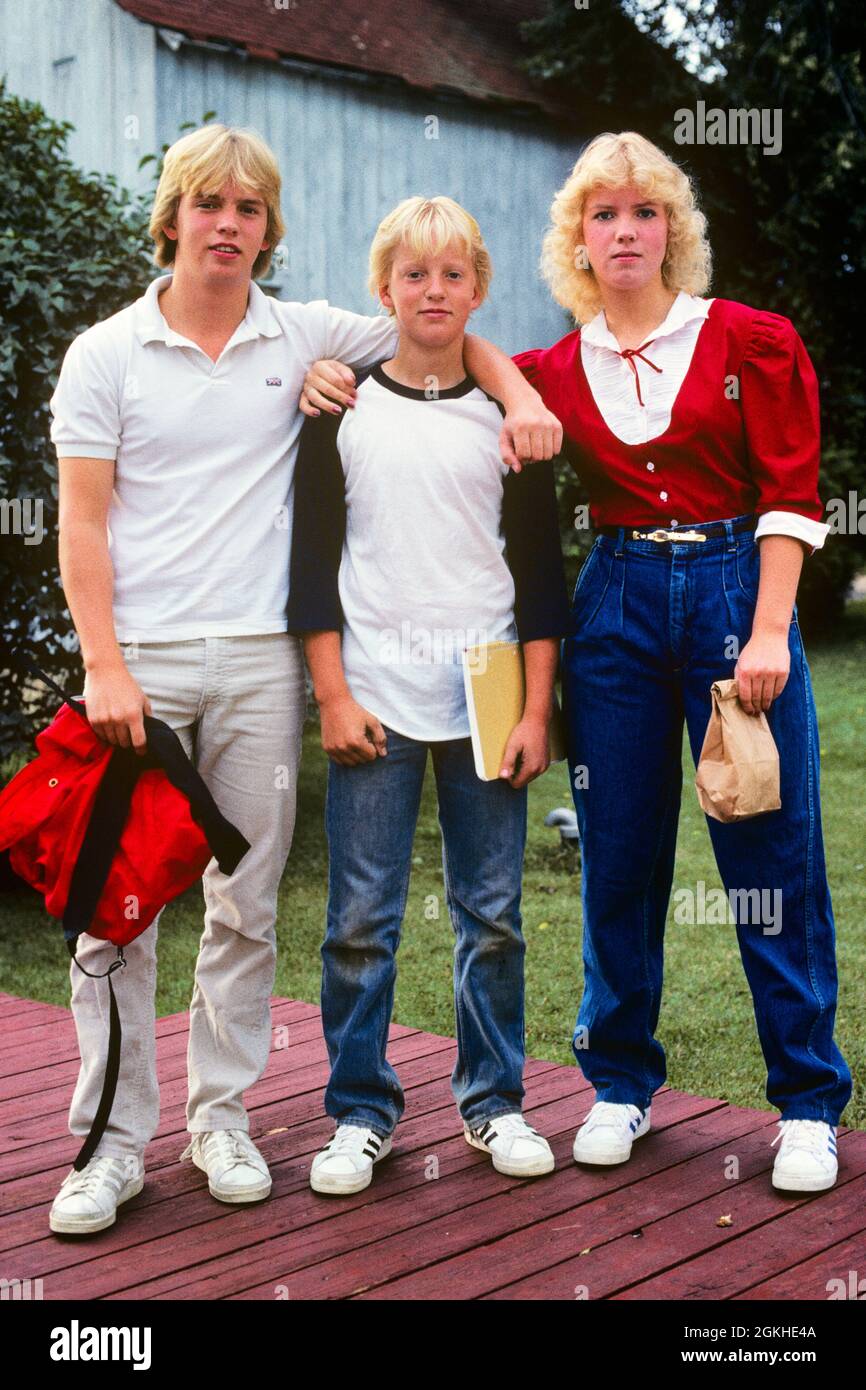 1980s THREE BLOND TEENAGERS BROTHERS SISTERS STANDING TOGETHER LOOKING AT CAMERA ON FIRST DAY OF SCHOOL  - ks21327 LLY001 HARS BROTHER OLD FASHION SISTER 1 JUVENILE STYLE BLOND FAMILIES LIFESTYLE FEMALES BROTHERS HEALTHINESS HOME LIFE COPY SPACE FRIENDSHIP FULL-LENGTH PERSONS CARING MALES TEENAGE GIRL TEENAGE BOY SNEAKERS SIBLINGS DENIM SISTERS EYE CONTACT HAPPINESS STYLES PRIDE HIGH SCHOOL SIBLING HIGH SCHOOLS CONNECTION CONCEPTUAL DNA STYLISH TEENAGED BLUE JEANS FAMILY RESEMBLANCE FASHIONS JUVENILES TOGETHERNESS CAUCASIAN ETHNICITY GENES OLD FASHIONED SEPTEMBER Stock Photo