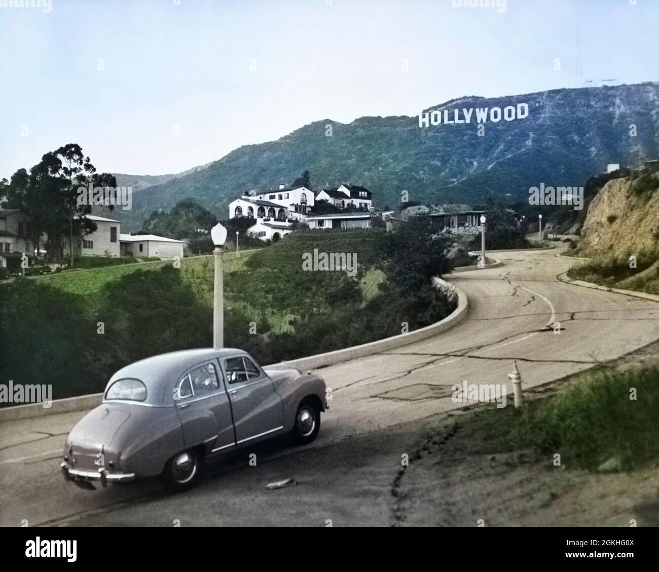 1950s AUSTIN CAR DRIVING UP ROAD IN THE HOLLYWOOD HILLS WITH HOLLYWOOD SIGN IN DISTANCE LOS ANGELES CALIFORNIA USA - q53014c CPC001 HARS COMMUNICATE HOLLYWOOD HILLS HOLLYWOOD SIGN ROADS 1923 LANDMARK LOS ANGELES OLD FASHIONED Stock Photo