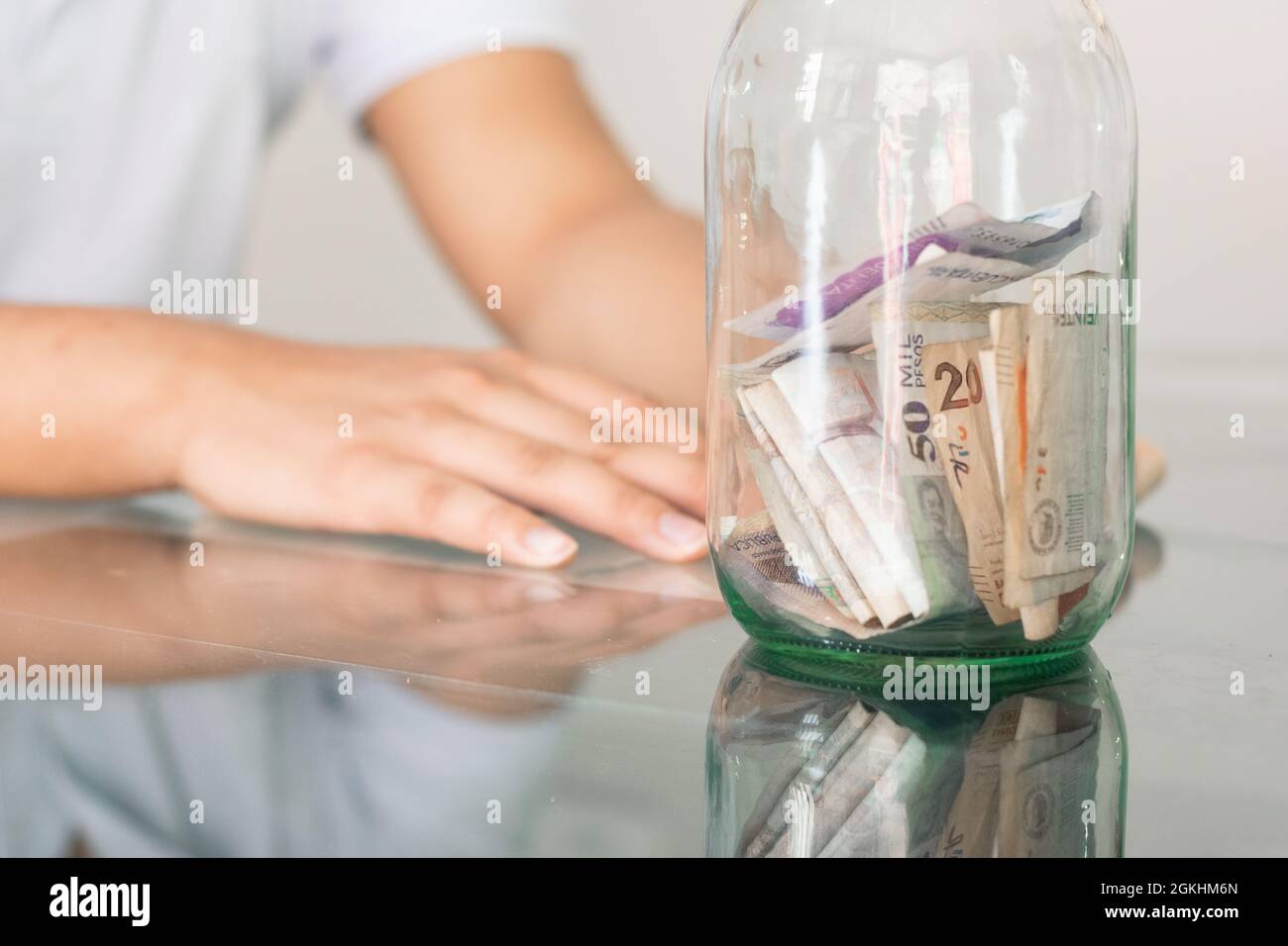 boy's hand next to his savings in a glass jar. young man next to his personal finances. bored student with a hand on his head. savings and finance con Stock Photo