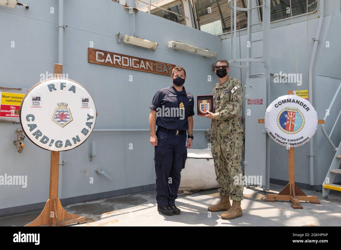 210426-AUN662-1194 ARABIAN GULF (April 26, 2021) – Royal Navy Cmdr. Jim Lovell, commander of Mine Warfare Battlestaff Red, left, presents a gift to Rear Adm. Curt Renshaw, deputy commander of U.S. Naval Forces Central Command and U.S. 5th Fleet, aboard Royal Fleet Auxiliary landing ship dock RFA Cardigan Bay (L 3009) after a mine countermeasures capability brief during exercise Artemis Trident 21 in the Arabian Gulf, April 26. Artemis Trident 21 is a multilateral mine countermeasures exercise between the UK, Australia, France and U.S., designed to enhance mutual interoperability and capabiliti Stock Photo