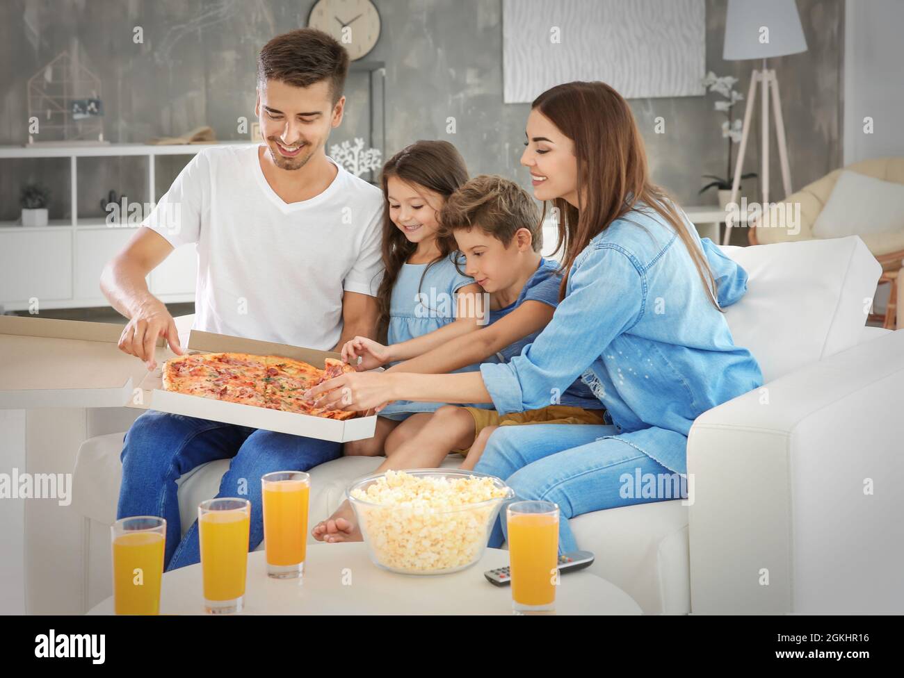 Happy family eating pizza while watching TV on sofa at home Stock Photo -  Alamy