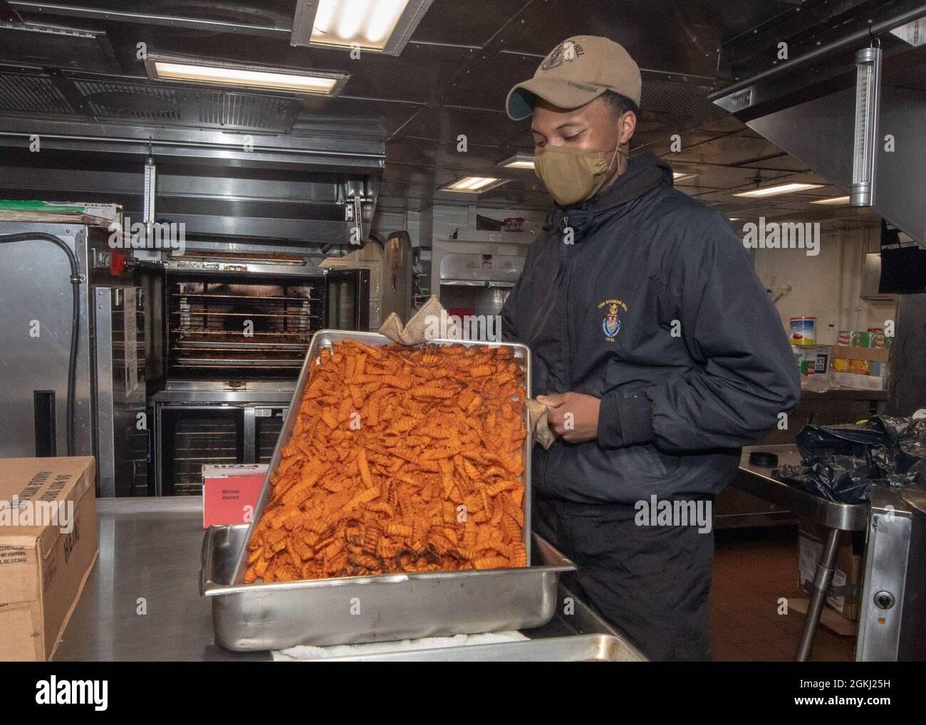 PACIFIC OCEAN (April 28, 2021) U.S. Navy Culinary Specialist Seaman Ethan Gardenhire, from Cleveland, puts sweet potato fries in a serving pan in the galley of the Ticonderoga-class guided-missile cruiser USS Bunker Hill (CG 52) April 28, 2021. Bunker Hill, part of the Theodore Roosevelt Carrier Strike Group, is on a scheduled deployment conducting routine operations in U.S. 3rd Fleet. Stock Photo