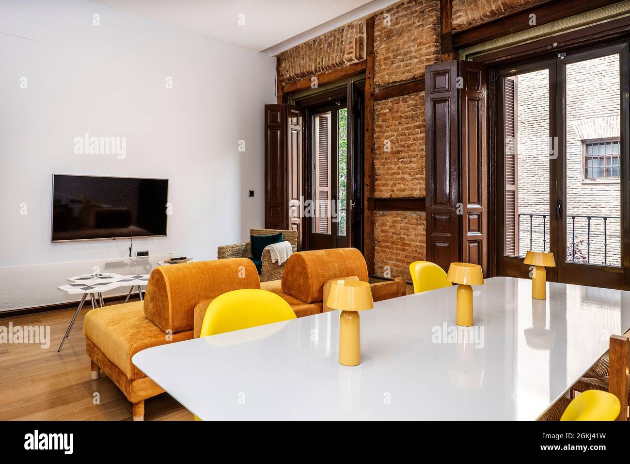 Large dining table in the foreground in a dining room with tv, large windows and exposed brick wall in an old Spanish building dedicated to vacation r Stock Photo