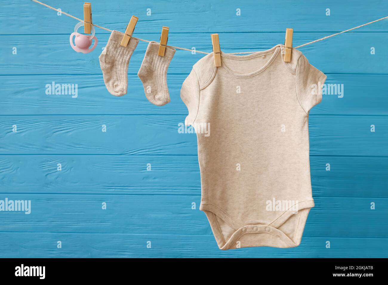 Baby clothes and pacifier hanging on rope against color wooden ...
