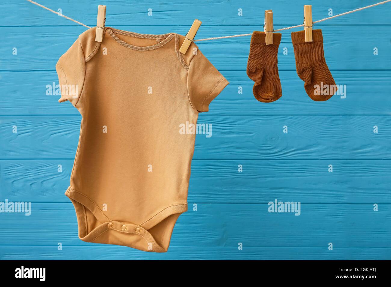 Baby clothes hanging on rope against color wooden background Stock ...