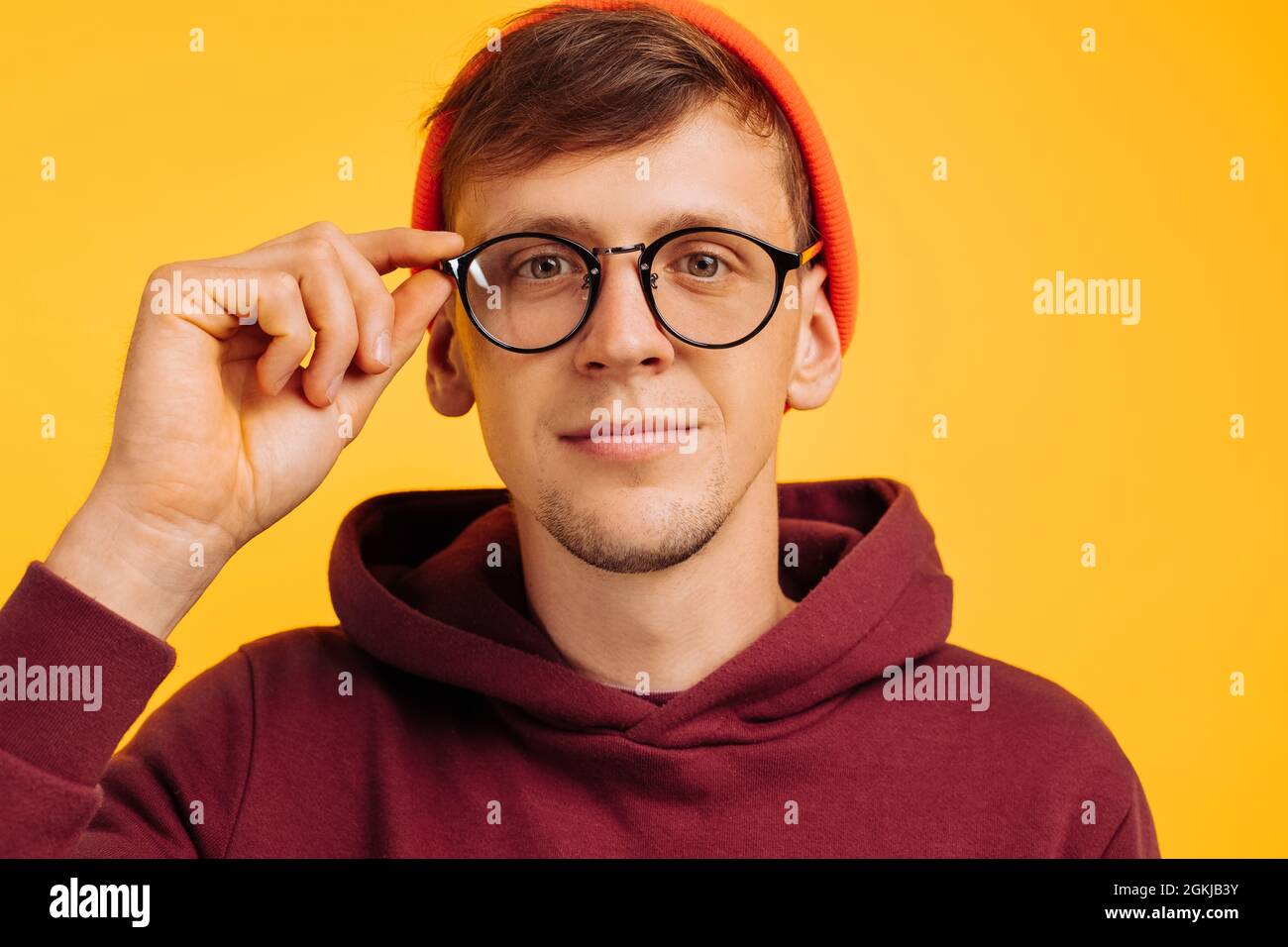guy has poor eyesight, a handsome guy in an orange hat and red light and glasses for vision squints, on a yellow background Stock Photo