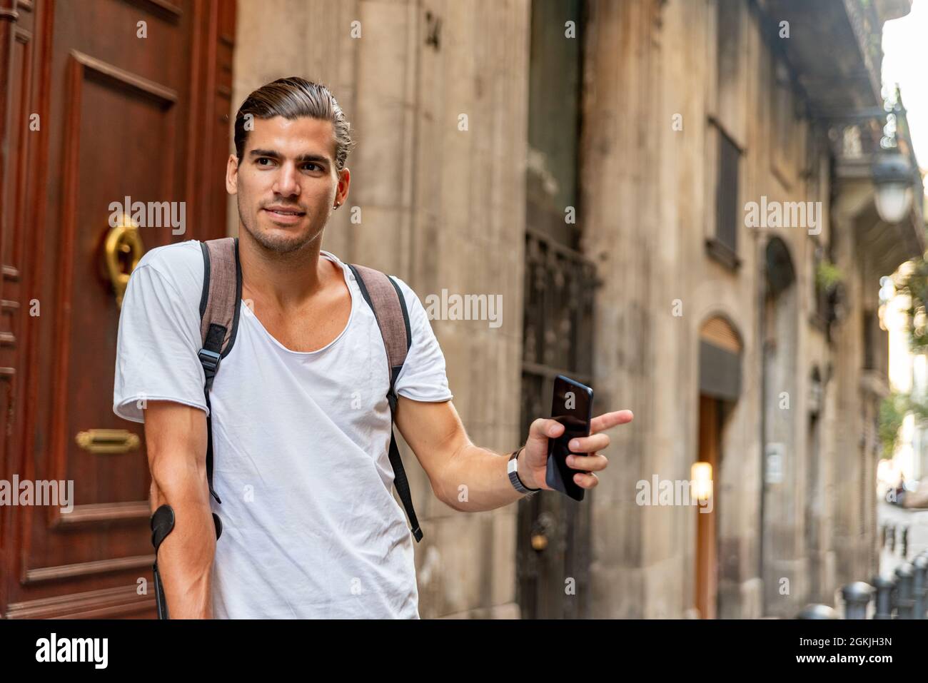 Young latin man with crutches stopping a taxi in the street Stock Photo