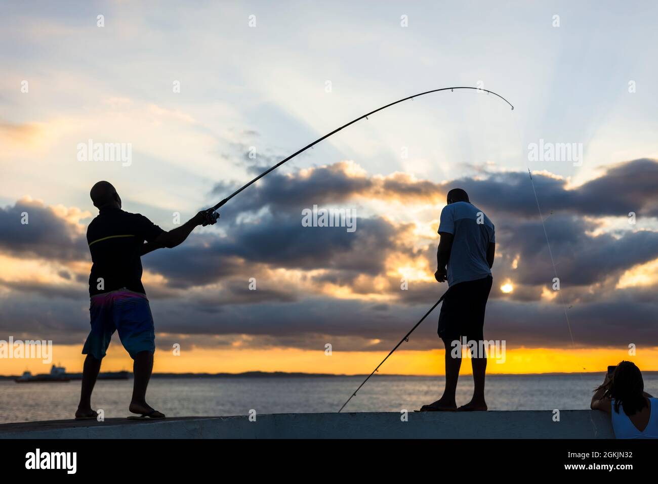 Salvador, Bahia, Brazil - May 23, 2021: Silhouette of fishermen with their poles at sunset. Stock Photo