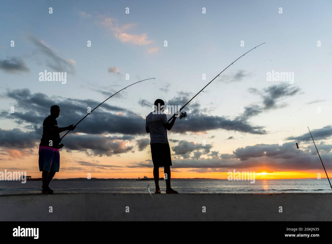 Salvador, Bahia, Brazil - May 23, 2021: Silhouette of fishermen with their poles at sunset. Stock Photo