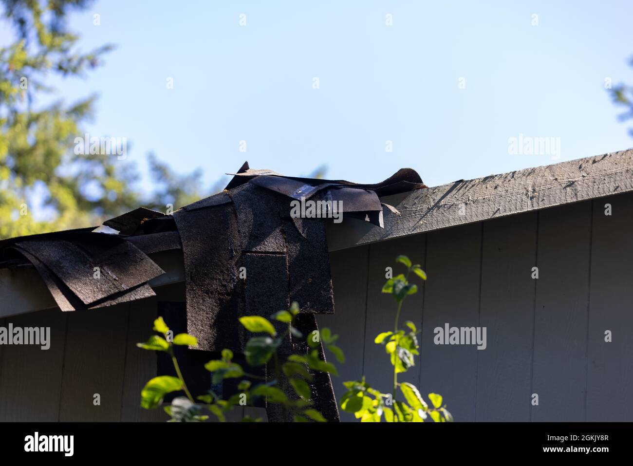 Old worn damaged shingles dangling over the edge of a roof piled up for