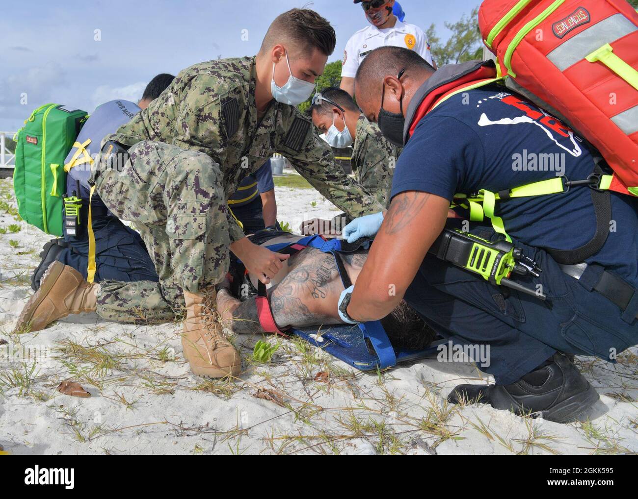 DIEGO GARCIA, British Indian Ocean Territory (May 12, 2021) – U.S. Navy Sailors along with first responders strap a wounded shark attack victim into a stretcher during a drill on Diego Garcia, May 12, 2021. U.S. Navy Support Facility Diego Garcia provides logistic, service, recreational and administrative support to U.S. and allied forces forward deployed to the Indian Ocean and Arabian Gulf. Stock Photo