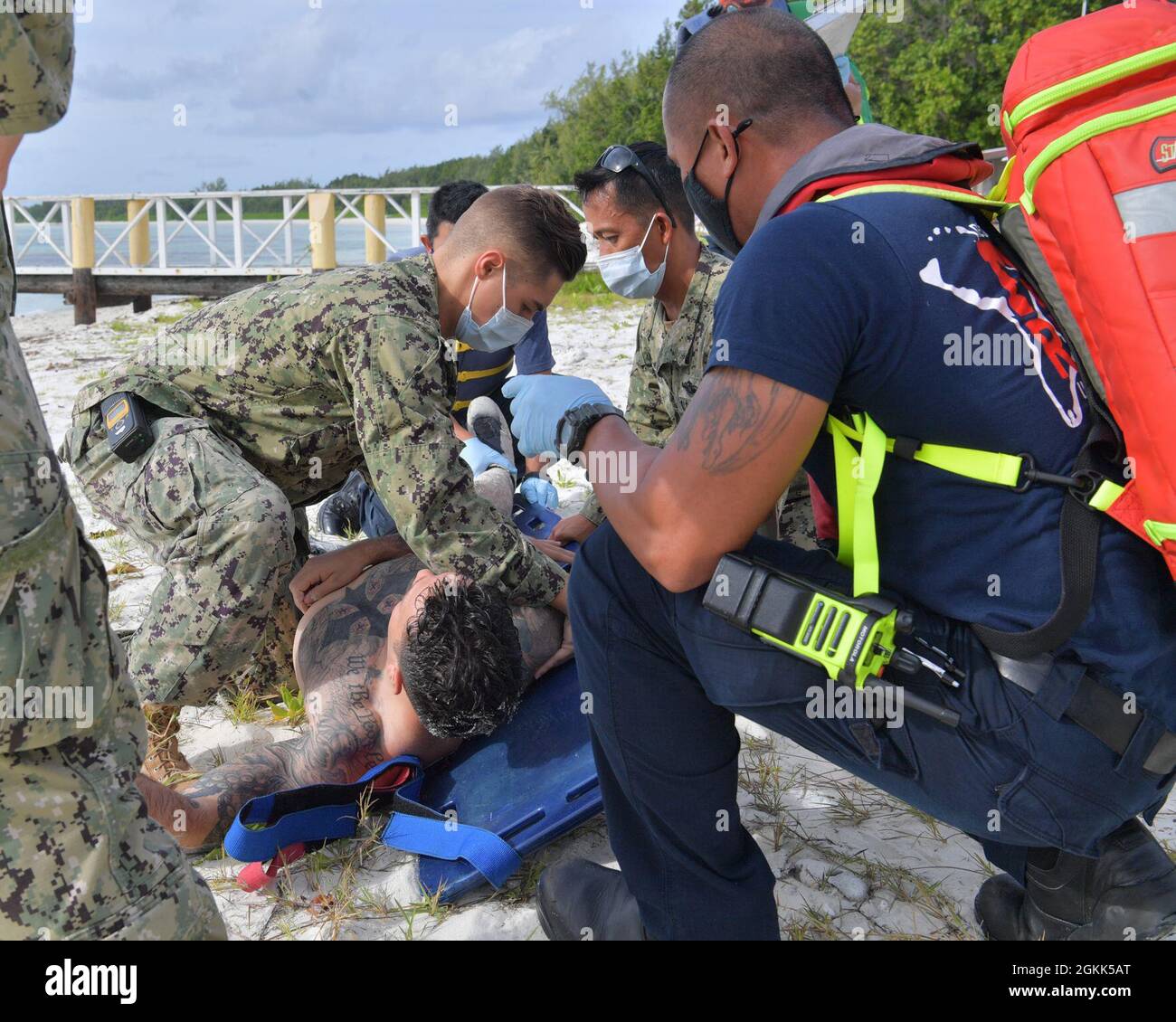 DIEGO GARCIA, British Indian Ocean Territory (May 12, 2021) – U.S. Navy Sailors along with first responders lift a wounded shark attack victim on to a stretcher during a drill on Diego Garcia, May 12, 2021. U.S. Navy Support Facility Diego Garcia provides logistic, service, recreational and administrative support to U.S. and allied forces forward deployed to the Indian Ocean and Arabian Gulf. Stock Photo