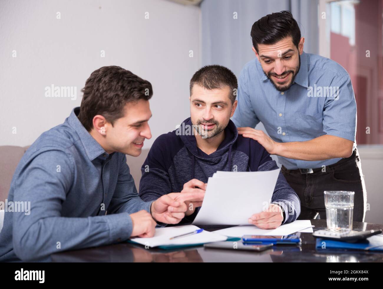 Three smiling men discussing papers at desk Stock Photo