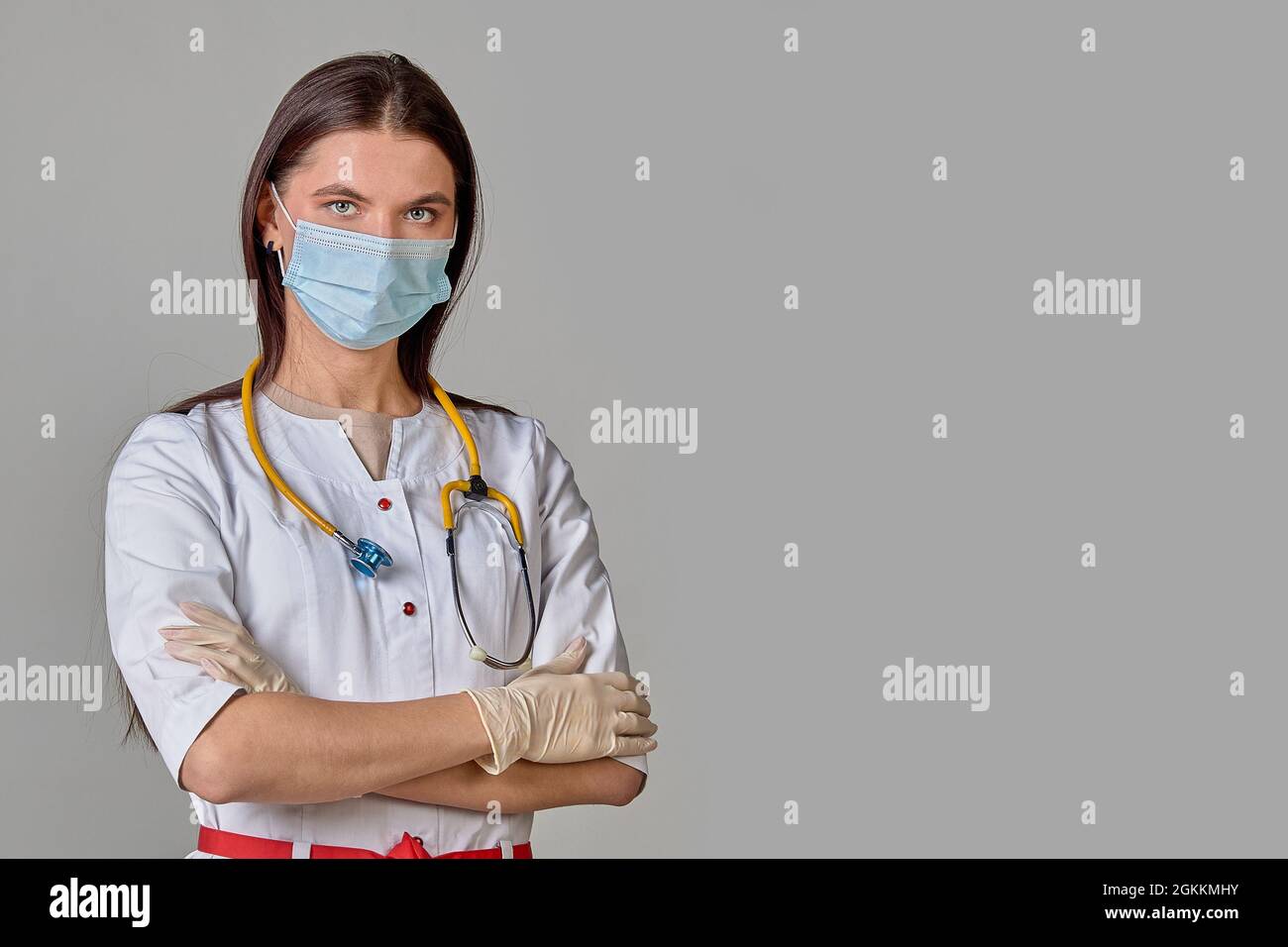 A young female doctor in a white coat with a stethoscope and a medical mask on a gray isolated background Stock Photo
