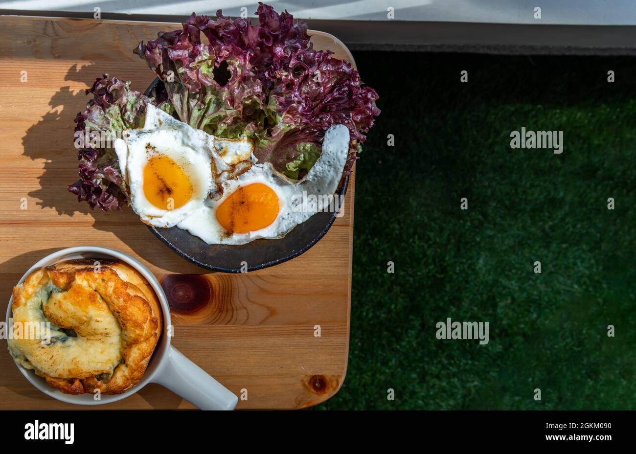 Breakfast with Spinach brioche, Two fried eggs, Oak Leaf lettuce on wooden table at balcony. Selective focuse. Stock Photo