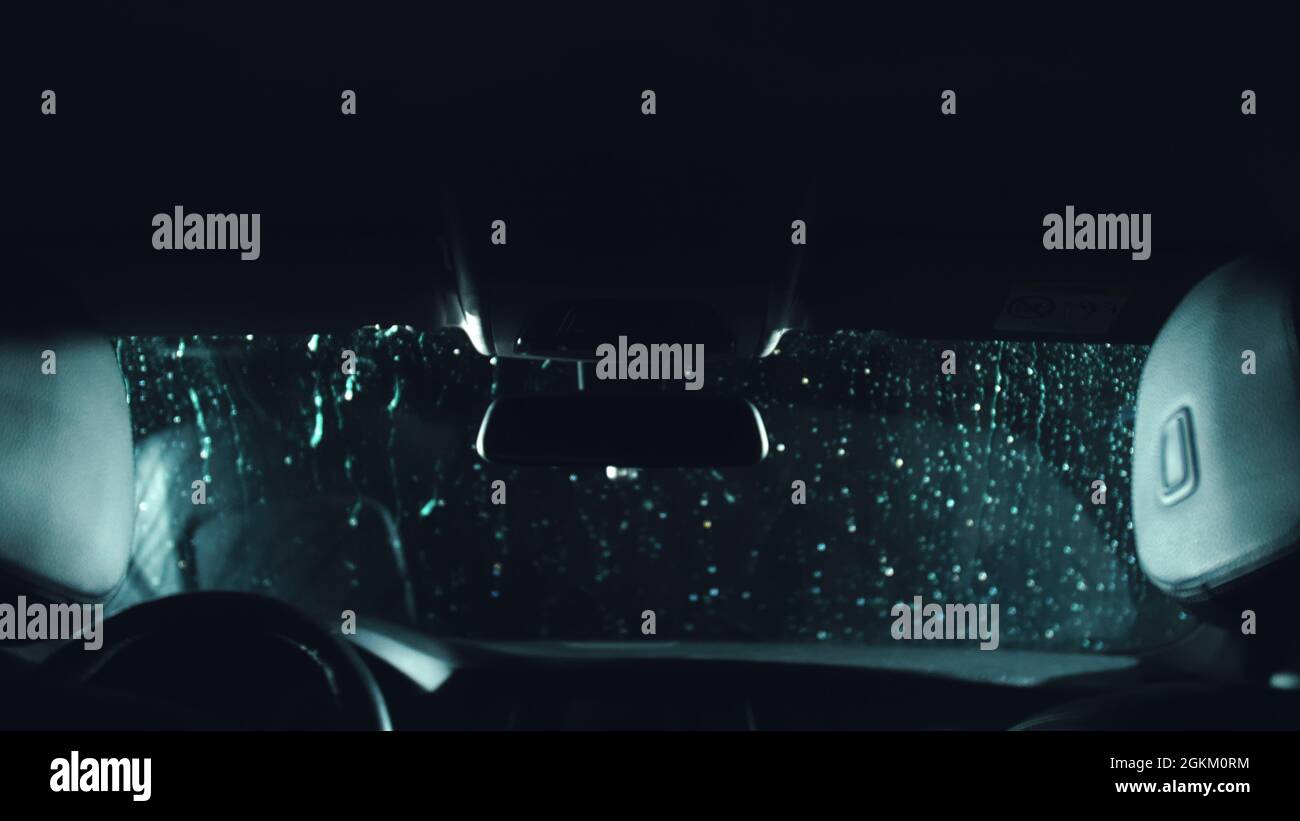 Drops flow down the windscreen. Inside view of a windshield car. Dark black cinematic picture. Process stage of polishing and washing a auto. Movement Stock Photo