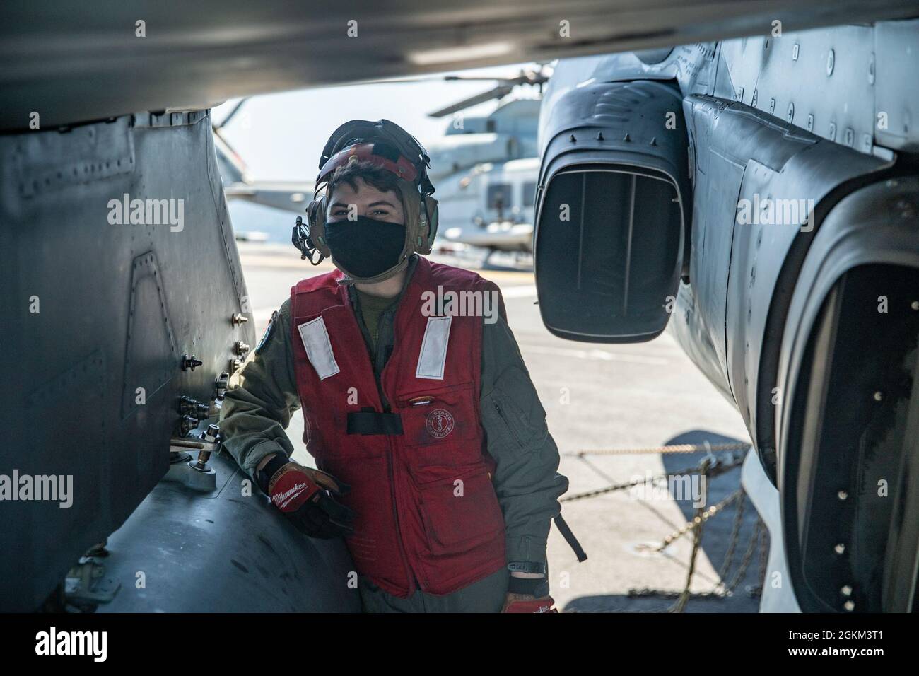 PACIFIC OCEAN (May 21, 2021) U.S. Marine Corps Cpl. Gigi Gruber, an ordnance quality assurance safety observer with Marine Attack Squadron (VMA) 214, 11th Marine Expeditionary Unit (MEU), poses for a photo beneath the wing of an AV-8B Harrier on the flight deck of amphibious assault ship USS Essex (LHD 2), May 21. Aside from equipping aircraft with munitions, Gruber’s responsibilities include inspecting aircraft and ordnance prior to takeoff to ensure that nothing will compromise the safety of the aircraft or pilot. Marines and Sailors of the 11th MEU and Essex Amphibious Ready Group (ARG) are Stock Photo