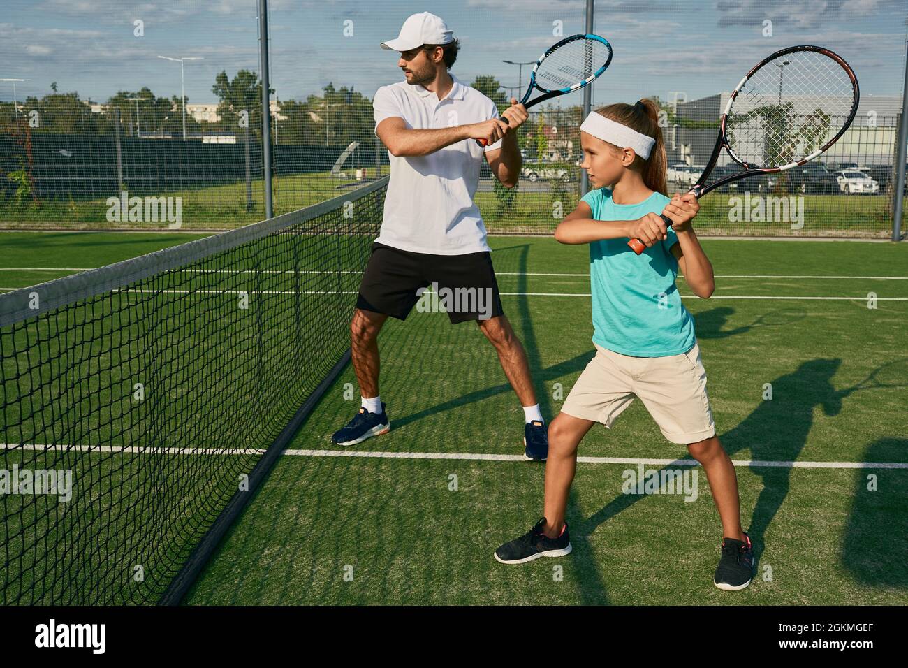Father is a tennis coach for his daughter. Female child is playing in tandem with her daddy in doubles tennis Stock Photo