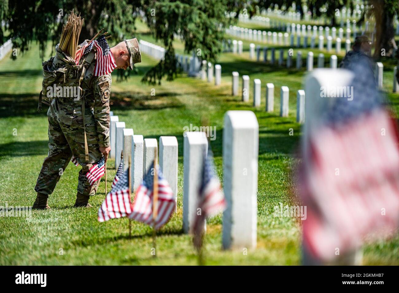 An airman assists in placing over 265,000 U.S. flags at every gravesite, columbarium court column, and niche wall column as part of Flags-In at Arlington National Cemetery, Arlington, Virginia, May 27, 2021.    For more than 50 years, soldiers from The Old Guard have honored our nation’s fallen military heroes by placing U.S. flags at the gravesites of service members buried at both Arlington National Cemetery and the U.S. Soldiers’ and Airmen’s Home National Cemetery just prior to the Memorial Day weekend. For the first time in 20 years, members from the U.S. Marine Corps, the U.S. Navy, the Stock Photo