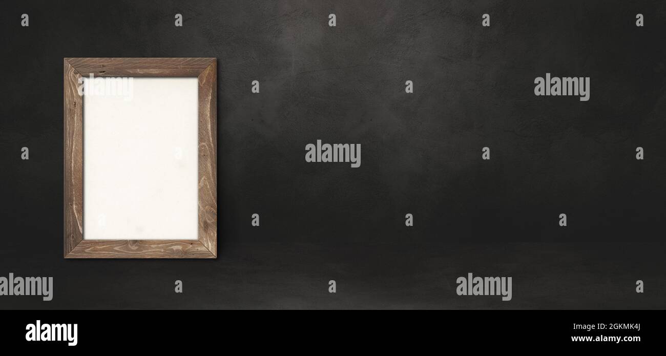 Wooden picture frame leaning on a black wall. Presentation mockup ...