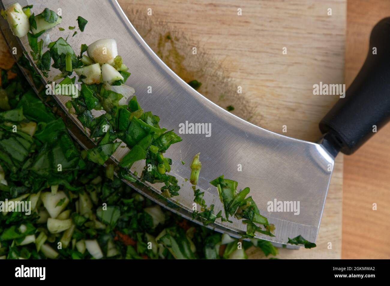 A close up of a double mezzaluna knife with garlic and basil on its